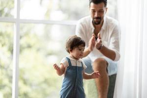 criança bonitinha conceito de família criança, bebê aprendendo a andar com pai e mãe para ajudar a cuidar e segurar a mão, primeiro passo com apoio dos pais na infância, pequeno retrato de amor menino em casa foto