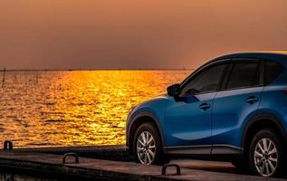 carro suv compacto azul com esporte e design moderno estacionado na estrada de concreto à beira-mar ao pôr do sol. tecnologia amiga do ambiente. tecnologia e negócios de carros elétricos. auto e automotivo híbridos. foto