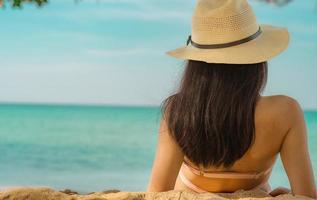 vista traseira da jovem asiática feliz em maiô rosa e chapéu de palha relaxar e desfrutar de férias na praia do paraíso tropical ao pôr do sol. garota na moda de férias de verão. modelo sexy de beleza. Ritmo de verão. foto