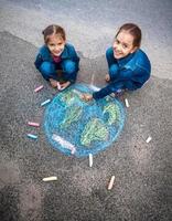 meninas sorridentes, desenhando a terra com giz na rua foto