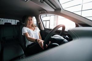 o que está por trás, olha no espelho. garota no carro moderno no salão. durante o dia dentro de casa. compra de veículo novo foto