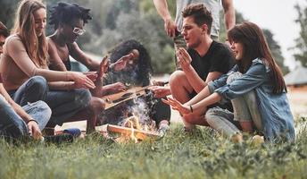 aquecimento pela fogueira. grupo de pessoas faz piquenique na praia. amigos se divertem no fim de semana foto