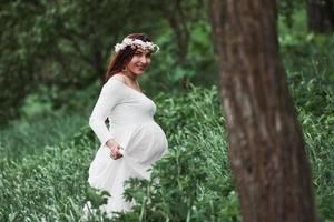 tendo um bom tempo. linda mulher grávida de vestido dar um passeio ao ar livre. morena positiva foto