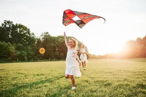 criança está sorrindo. mãe e filha se divertem com pipa no campo. natureza bela foto