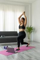 ajuste o exercício de treino online desportivo jovem asiático em casa. menina saudável ativa desfrutar de esporte pilates yoga treinamento de fitness no computador portátil alongamento no tapete de ioga assistindo aula de vídeo foto