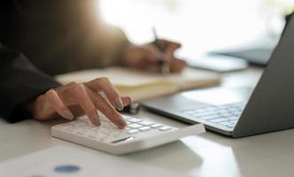 feche o contador trabalhando na mesa no escritório usando a calculadora para calcular o orçamento enquanto toma nota no bloco de notas. conceito de finanças e contabilidade foto