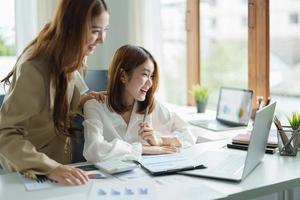 duas mulheres sentam-se na mesa, sentem-se eufóricas, ganham loteria online, mulher asiática feliz, muito feliz, recebe e-mail no laptop sendo promovido no trabalho, garota birracial espantada ao ler boas notícias no computador. foto