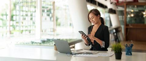 mulher asiática de negócios usando telefone celular durante a verificação de um e-mail ou mídia social na internet. conceito financeiro contábil. foto