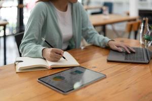 mulher asiática escrevendo fazendo lista tomando notas no bloco de notas trabalhando ou aprendendo no laptop dentro de casa - curso educacional ou treinamento, seminário, conceito on-line de educação foto