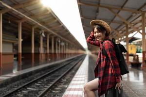 feliz viajante da ásia sentindo felicidade antes de viajar na estação de trem, viagens de verão e conceito de estilo de vida foto