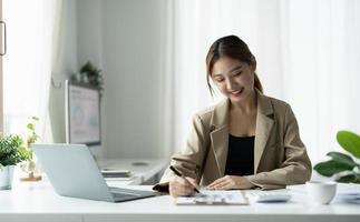 Mulher asiática de negócios usando smartphone para fazer finanças matemáticas na mesa de madeira no escritório, impostos, contabilidade, conceito financeiro foto