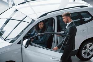 você vai sentir conforto. cliente do sexo feminino e empresário barbudo elegante moderno no salão de automóveis foto