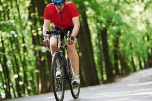 olhar concentrado. ciclista de bicicleta está na estrada de asfalto na floresta em dia ensolarado foto
