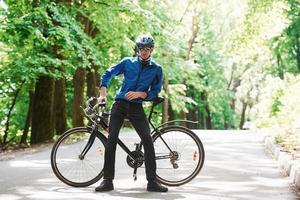 apaixonado pelo seu equipamento. ciclista de bicicleta está na estrada de asfalto na floresta em dia ensolarado foto