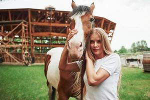 mulher com roupas casuais. garota feliz com seu cavalo no rancho durante o dia foto