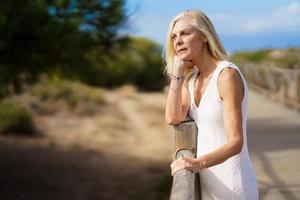 mulher de 60 anos, apoiando-se em cercas de madeira na areia de uma praia tropical. foto