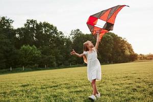 é bom aqui. garota feliz em roupas brancas divirta-se com pipa no campo. natureza bela foto