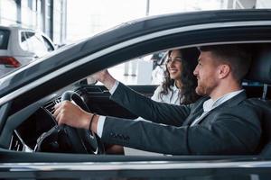 isso parece bom. lindo casal bem sucedido tentando carro novo no salão de automóveis foto