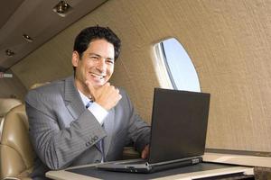 homem de negócios usando o laptop no avião, sorrindo, close-u