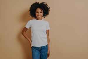 alegre fêmea africana em camiseta branca e jeans expressando emoções positivas, posando no estúdio foto