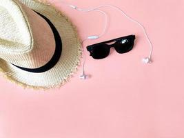 chapéu tecido, fone de ouvido e óculos de sol no verão de fundo de cor rosa pastel foto
