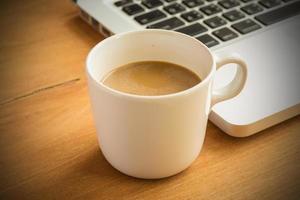 xícara de café com leite quente e laptop sobre fundo de madeira e textura. foto