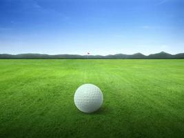 fechar a bola de golfe no campo de grama verde e bandeira de golfe vermelha no fairway verde com lindo céu azul foto