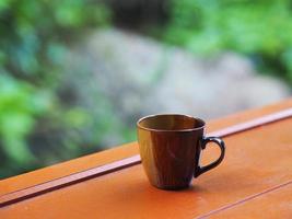 xícara de café marrom na mesa de madeira bokeh com natureza desfocada de fundo foto