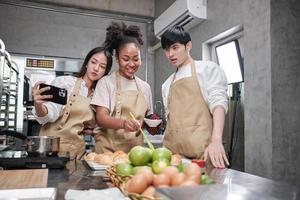 três jovens estudantes na aula de culinária usam aventais prazer enquanto tiram foto de selfie com o celular na cozinha, sorrindo e rindo, preparando ovos e frutas, aprendem juntos um curso de culinária divertido.