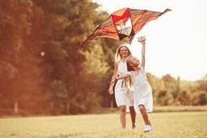 dia ensolarado de verão. mãe e filha se divertem com pipa no campo. natureza bela foto