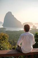 homem viajante feliz aproveite o ponto de vista da baía de phang nga, turista sozinho sentado e relaxando no mesmot nang ela, perto de phuket, no sul da tailândia. conceito de viagem, viagem e férias de verão no sudeste da ásia foto