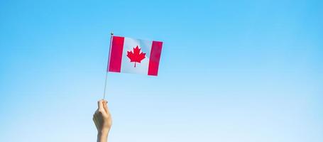 mão segurando a bandeira do Canadá no fundo do céu azul. dia do canadá e conceitos de celebração feliz foto