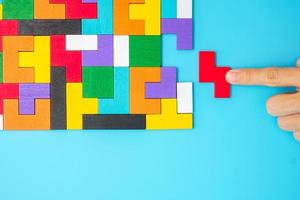 mão conectando peças de quebra-cabeça de madeira coloridas sobre fundo azul, bloco de forma geométrica. conceitos de pensamento lógico, enigma, soluções, racional, estratégia, dia mundial da lógica e educação foto