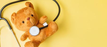 estetoscópio com boneca de urso em fundo amarelo para apoiar a vida e a doença da criança. setembro mês de conscientização do câncer infantil, conceito de saúde e seguro de vida foto