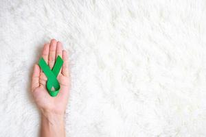 mão segurando a fita verde para apoiar as pessoas vivas e doentes. fígado, ducto biliar da vesícula biliar, câncer de rim e conceito de mês de conscientização do linfoma foto