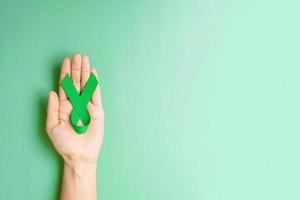 mão segurando a fita verde para apoiar as pessoas vivas e doentes. fígado, ducto biliar da vesícula biliar, câncer de rim e conceito de mês de conscientização do linfoma foto