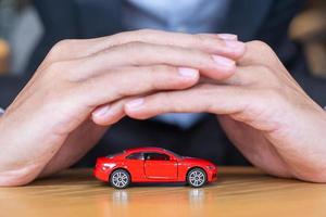 capa de mão de empresário ou brinquedo de carro vermelho de proteção na mesa. conceito financeiro, dinheiro, refinanciamento e seguro de carro foto