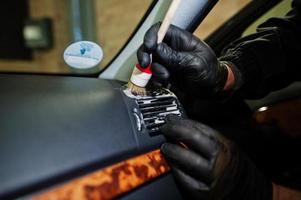 homem de uniforme e respirador, trabalhador do centro de lavagem de carros, escova de limpeza interior do carro. conceito de detalhamento do carro. foto