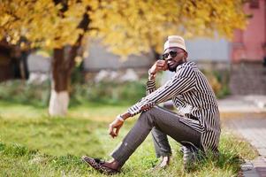 retrato de homem afro-americano elegante preto no chapéu e óculos de sol contra o fundo de outono ensolarado outono. pessoas ricas da áfrica em trajes tradicionais. foto