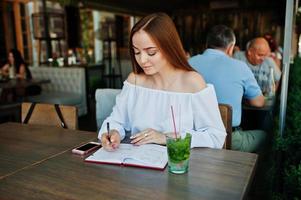 retrato de uma linda jovem empresária bem sucedida escrevendo algo em seu caderno vermelho enquanto está sentado em um café. foto