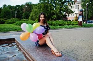 linda menina morena na rua da cidade com balões nas mãos. foto
