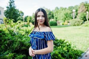 linda menina morena na rua da cidade usa vestido listrado azul. foto