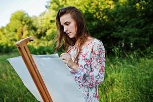 retrato de uma jovem atraente em vestido longo pintando com aquarela na natureza. foto