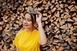 jovem garota engraçada com maquiagem brilhante, como princesa de conto de fadas, usar camisa amarela e coroa contra fundo de madeira. foto