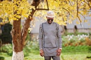 retrato de homem afro-americano elegante preto no chapéu e óculos de sol contra o fundo de outono ensolarado outono. pessoas ricas da áfrica em trajes tradicionais. foto