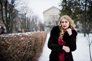 elegância loira em vestido de noite vermelho e casaco de pele nas ruas da cidade em dia de inverno. foto