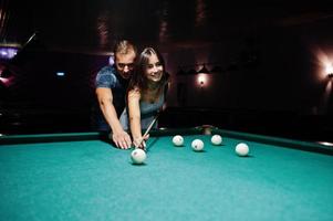 mulher de vestido jogando sinuca com um homem em um pub. foto