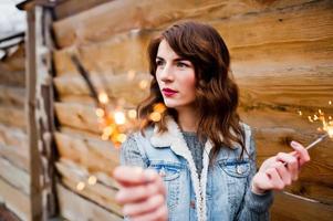 retrato de menina morena de jaqueta jeans com luzes de bengala nas mãos. foto