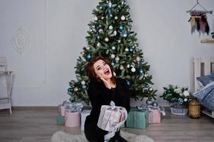 menina desgaste na árvore de ano novo de fundo preto com caixas de presentes no estúdio. feliz conceito de férias de inverno. foto