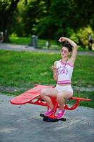 garota esportiva usar shorts brancos e camisa fazendo exercícios em simuladores ao ar livre no parque. foto